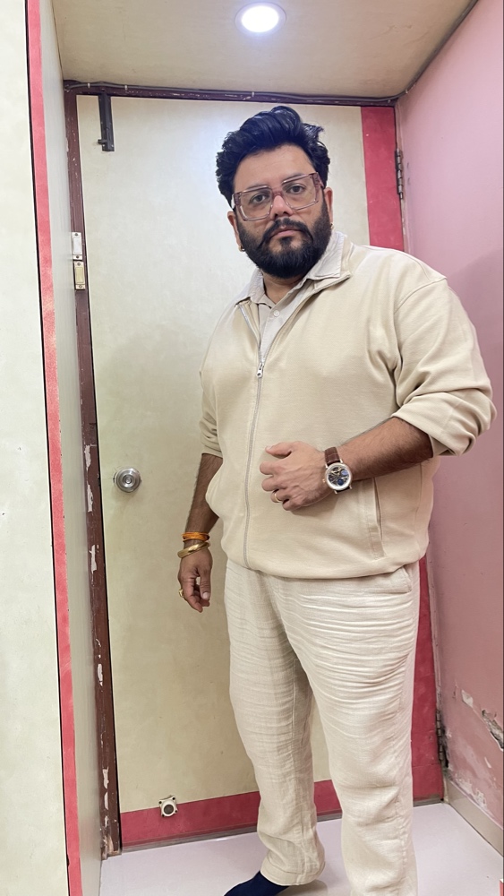 Niraj Choksi standing in a doorway, wearing a cream jacket and trousers